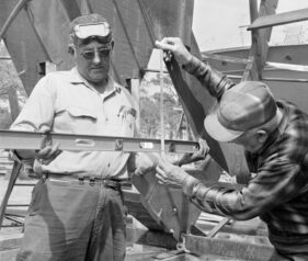 black and white picture of 2 men. One is holding a level and the other is holding a measurement tool in front of the level
